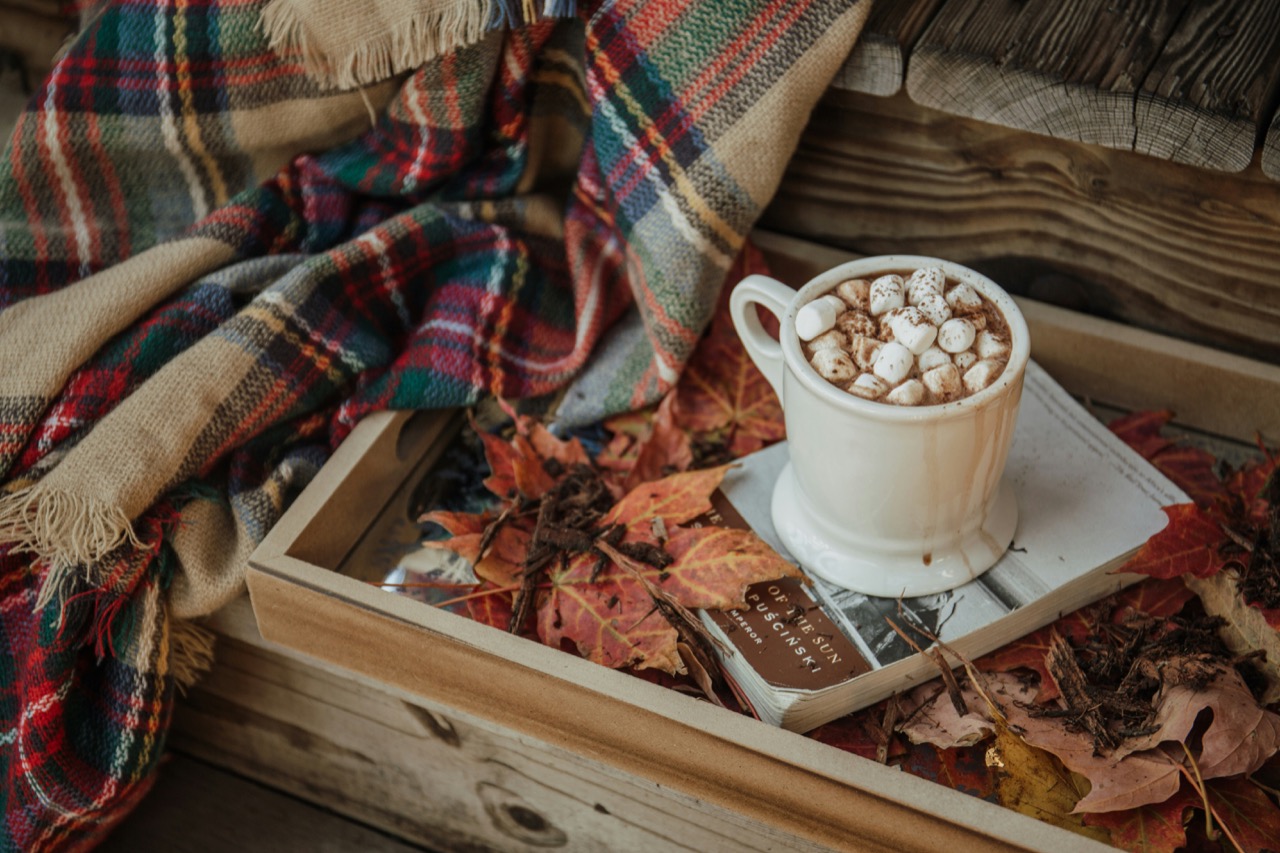 紅葉した落ち葉とブランケット、温かい飲み物が置かれた秋の情景