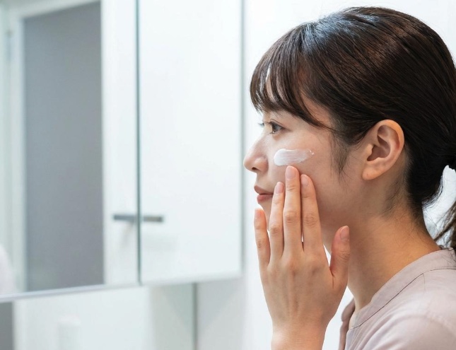 鏡の前で首元に日焼け止めを塗っている女性の様子