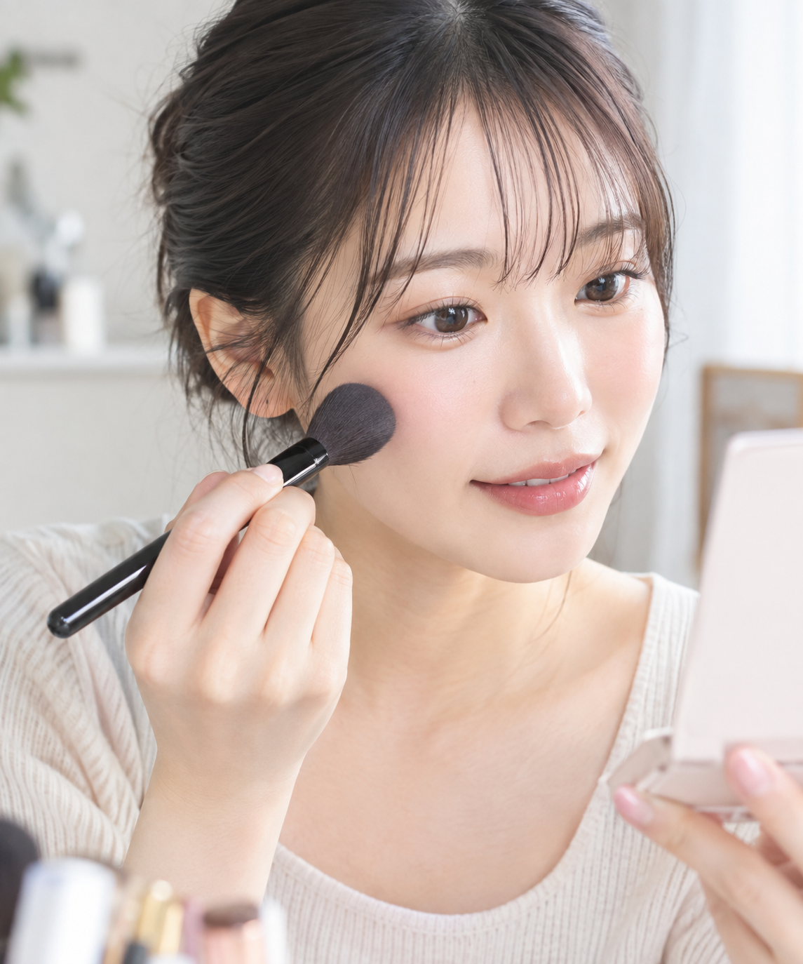 チークブラシで頬にメイクを乗せる女性の手元